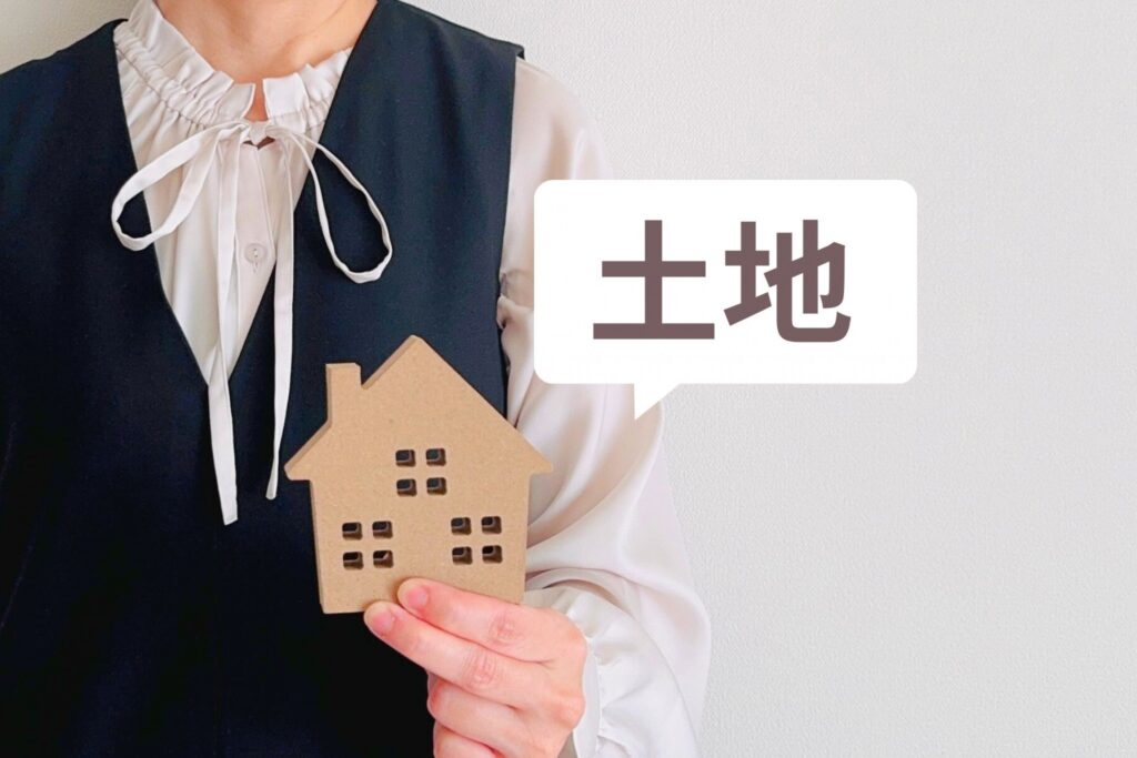 木の家モチーフを手にする女性と「土地」と書かれた吹き出しのイラスト。不動産購入や土地探しをイメージするカット。